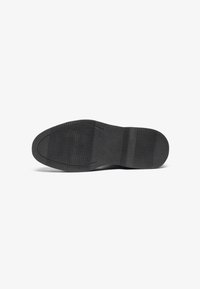 Semelle de chaussure en caoutchouc noir avec une texture adhérente, présentant des zones lisses et striées ainsi que des bords arrondis pour la stabilité.