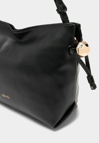 Bolso de hombro negro de cuero con textura suave, que presenta un adorno geométrico dorado y un diseño ligeramente caído.