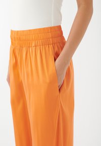 Orange byxor med elastisk midja och sidofickor, med en slät, glänsande yta och en lös, avslappnad passform.