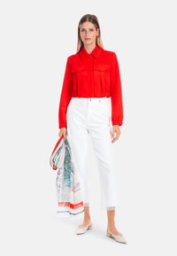 Red collared blouse with long sleeves and two front pockets, paired with white cropped pants featuring lace trim and a decorative scarf.