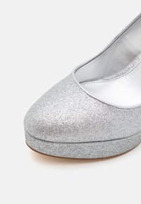 Chaussure à plateforme pailletée argentée avec bout arrondi et doublure intérieure lisse sur fond clair.