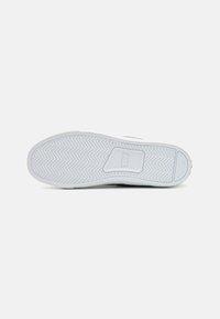 Fehér sneaker talp halszálka mintával, texturált gumiból készült, és egy márkajelzés található a sarkánál.