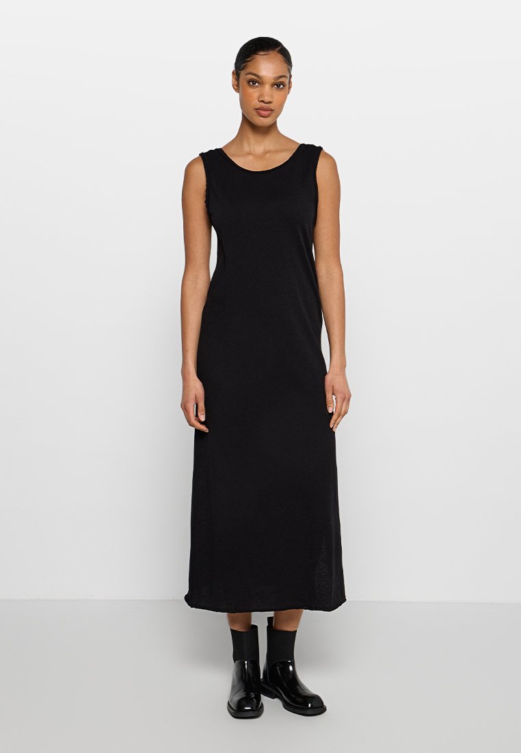 Schwarzes ärmelloses Maxikleid mit rundem Ausschnitt, aus glattem Stoff gefertigt. Bietet eine lässige Passform und einen seitlichen Schlitz. Trägt schwarze Knöchelstiefel.