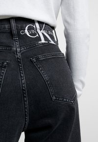 Černé džíny z denimu s vysokým pasem, na pásku výrazné logo Calvin Klein a dvě zadní kapsy s výrazným prošíváním.