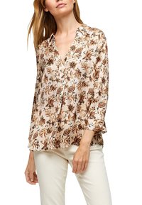 Blouse à imprimé floral en tissu léger, présentant un col en V, une fermeture à boutons et des manches trois-quarts avec une coupe ample. Base beige avec des accents marron.
