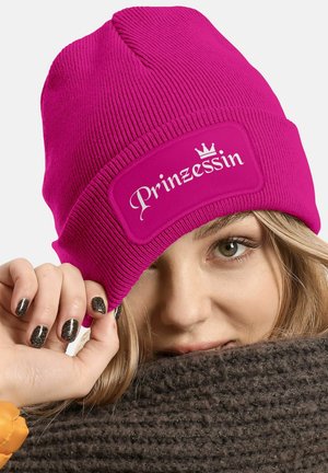 Bright pink knitted beanie with a textured finish. Features a white rectangular patch labeled "Prinzessin" with a small crown graphic.
