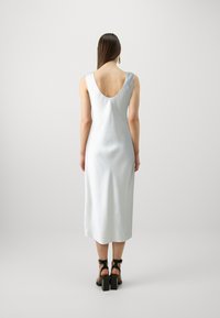 Rochie midi din satin de culoare albastru pal, cu spate decupat, siluetă dreaptă și textură netedă. Purtați cu sandale negre cu toc masiv.