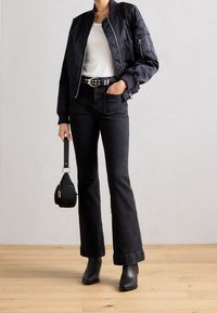 Černá bomber jacket se žebrovanými manžetami, bílý tričko, rozšířené černé džíny, opasek s cvočky a robustní černé boty na podpatku. Malá černá kabelka.