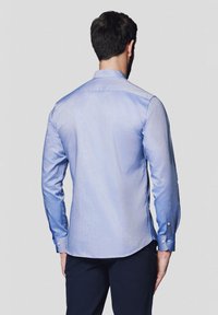 Jasnoniebieska koszula z długim rękawem o subtelnej fakturze, z wywijanym kołnierzykiem i zapinanymi mankietami, z zaokrąglonym dołem i gładkim wykończeniem.
