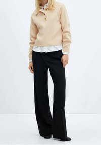 Vaalea beige neulepusero nappikauluksella, valkoisen paidan päällä. Yhdistetty löysiin mustiin housuihin.