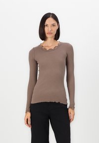 Bruine geribbelde longsleeve top met een geschulpte kanten halslijn en zoom. Heeft een aansluitend ontwerp en textiel met een textuur. Gecombineerd met zwarte broeken.