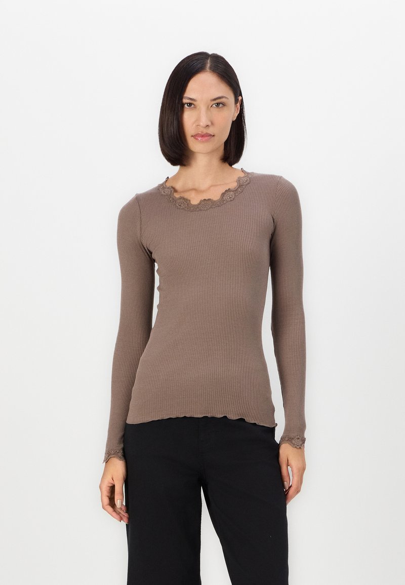 Bruine geribbelde longsleeve top met een geschulpte kanten halslijn en zoom. Heeft een aansluitend ontwerp en textiel met een textuur. Gecombineerd met zwarte broeken.