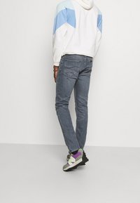Ljusgrå jeans med slim fit, kombinerat med en vit hoodie med blå detaljer. Skorna är flerfärgade sneakers med texturerade sulor.