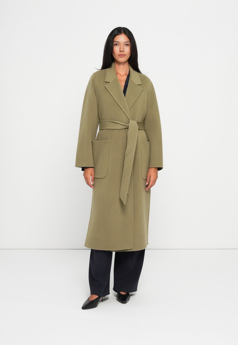 Cappotto in lana verde oliva con vita a cintura, ampi risvolti e due tasche frontali. Presenta maniche lunghe e un design lungo fino al polpaccio.