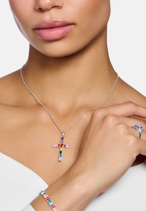 Silver cross pendant necklace with multicolored rectangular gemstones. Worn with a matching gemstone ring and bracelet. Smooth skin tone background.