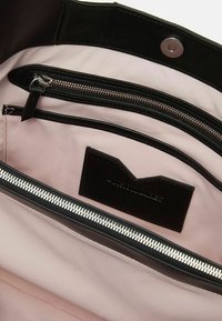 Interno in pelle nera di una borsa, con una fodera in tessuto rosa chiaro a contrasto, una tasca con zip e una piccola etichetta nera con dettagli del logo.