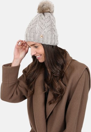 Knit beige beanie with a cable design, featuring a fur pom-pom on top and a small wooden logo accent. Soft texture and warm fit.