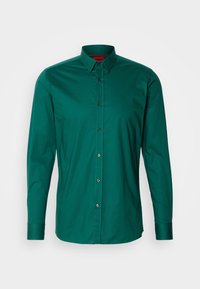 Chemise verte à manches longues en tissu lisse, dotée d'un col classique, d'une fermeture à boutons et de boutons foncés sur le devant.