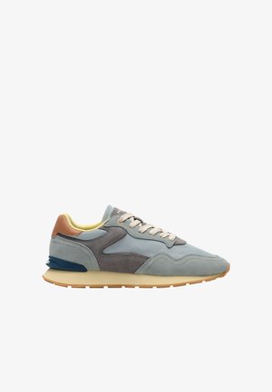 Zapatilla deportiva de ante gris y azul con suela beige, cordones crema y lengüeta trasera de cuero marrón, mostrada en perfil lateral.
