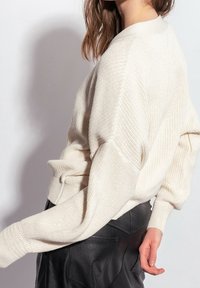 Smetanově barevný pletený svetr s volnějším střihem, doplněný žebrovanými manžetami a texturovaným vzorem. Kombinován s černou koženou sukní.