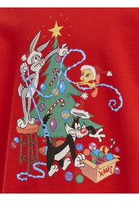 Tissu rouge présentant une scène de dessin animé avec un sapin de Noël vert, des ornements colorés et des personnages enchevêtrés dans des guirlandes lumineuses bleues.