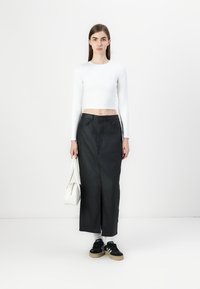 Fehér, hosszú ujjas cropped top, magas derékú fekete farmer szoknya elöl hasítékkal, fekete sportcipővel és fehér kézitáskával párosítva.