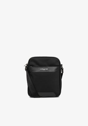 Zwarte stoffen schoudertas met een gladde textuur, voorzien van een ritssluiting, voorkoas en een verstelbare schouderband, gebrandmerkt met "Lancaster Paris."