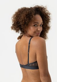 Soutien-gorge noir en dentelle dans le dos, avec bretelles réglables et fermeture à crochets. Design en tissu lisse avec de fins détails et des accents texturés.