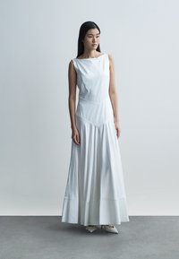 Abito lungo bianco senza maniche con scollo dritto, corpetto aderente e gonna svasata. Tessuto liscio con una sottile texture e design pulito.