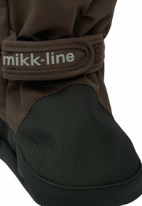 Acercamiento de una bota impermeable marrón y negra con punta texturizada y correa ajustable etiquetada como "mikk-line" para un ajuste seguro.