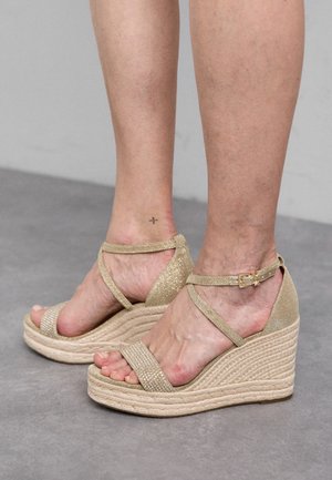 Sandales à semelle en jute tressé, avec des brides métalliques dorées et une boucle au niveau de la cheville. Tige texturée avec des accents pailletés.