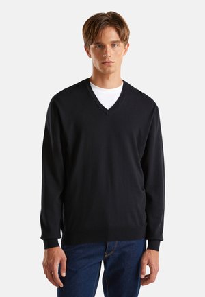 Zwarte V-halstrui in zachte stof met lange mouwen en geribbelde manchetten, gedragen over een wit T-shirt, gecombineerd met donkere jeans.
