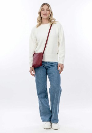 Cream-colored, fluffy sweater, loose blue jeans, and white sneakers. Red crossbody bag features textured material and a long strap.
