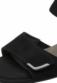 Schwarze Wildleder-Sandale mit breitem Klettverschluss, grauem Innenfutter und metallischem Akzent. Verfügt über eine flache Sohle und genähte Details.