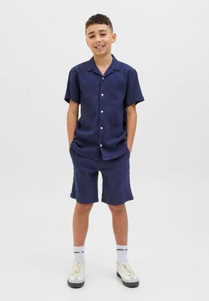 Marinblå kortärmad skjorta och matchande shorts i strukturerad tyg. Inkluderar vita knappar och avslappnad passform. Bärs med vita sneakers.