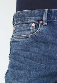 Tmavě modré džínové kalhoty s texturovaným povrchem, měděnými kovovými doplňky, pěti kapsami a standardním pasem.