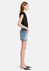 Maglietta nera a maglia con maniche corte, abbinata a pantaloni corti in denim blu e mule con tacco a punta nera. Silhouette semplice e aderente con costine.