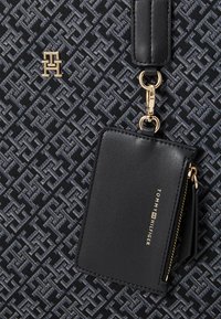 Black fabric handbag with a geometric pattern in dark blue. Features a gold logo and a detachable black leather cardholder with zipper.