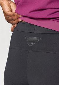 Zwarte legging met een soepele, rekbare stof, hoge tailleband en een matte logo-accent aan de achterkant. Zichtbare perforaties verbeteren de ademend vermogen.