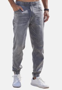 Pantalons de jogging en denim gris avec une taille élastique, des poches latérales et des poignets fuselés, associés à des sneakers blanches.