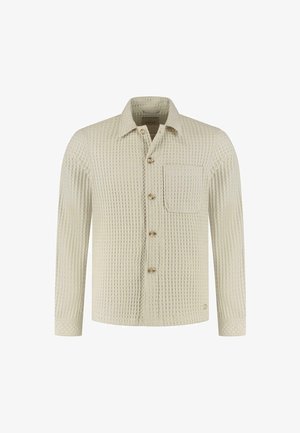 Camicia button-up color crema con un motivo a waffle testurizzato, taschino sul petto singolo e bottoni dorati. Maniche lunghe con polsini abbottonati.