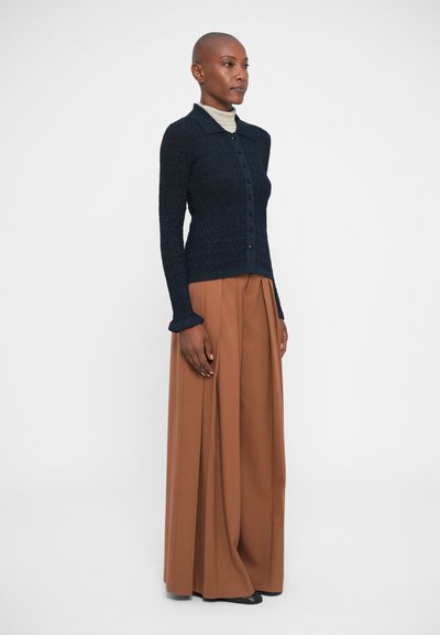 Cardigan en tricot navy avec col, fermeture à cinq boutons et poignets côtelés, associé à un pantalon large taille haute marron.