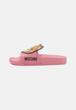 Vaaleanpunainen kuminen liukusandaali, jossa on karhukuva ja "Moschino"-brändäys remmissä. Pohjassa on tekstuuripinta mukavuutta varten.