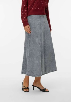 Gonna di jeans in grigio sbiadito, design a trapezio con cuciture visibili, abbinata a un cardigan bordeaux a pois e sandali neri con tacco.