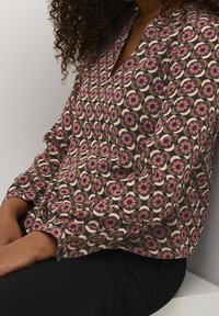Langärmlige Bluse mit geometrischem Muster in Pink- und Beigetönen, aus einem weichen Stoff gefertigt, mit V-Ausschnitt und Knopfdétails.