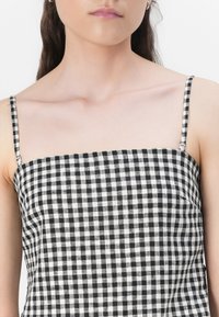 Svart og hvit gingham-bluse med tynne stropper, firkantet utringning og flat tekstur. Stoffet har et rutet mønster.