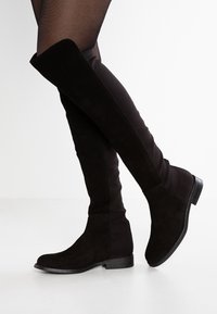 Svarta över-knän stövlar i mocka och tyg, med en slät yta, platt klack och rund tåkonstruktion.