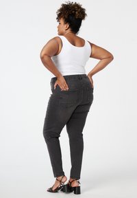 Grijze denim jeans met een slim fit en elastische tailleband, voorzien van achterzakken en een lichte tapering bij de enkel. Ggedragen met een witte tanktop.