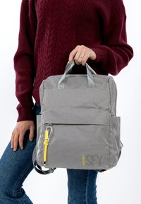 Grijze textuurrugzak met dubbele bovenhandvatten, extern vak, gele ritstrekker en verstelbare schouderbanden. Compact ontwerp, functionele indeling.