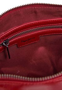 Roter Tascheninnerraum mit Stofffutter, sichtbarem Reißverschlussfach und Pepe Jeans London-Logo auf einem roten Lederschild innen.